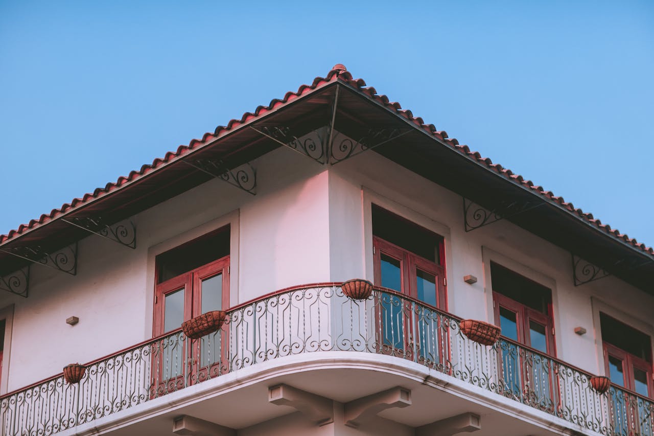 Low-angle view of a traditional house with ornate balcony, red windows, under a clear blue sky.