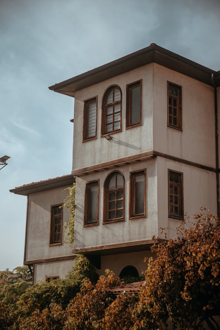 The Art of Drawing Readers In: Your attractive post title goes here A rustic two-story house with vintage architecture surrounded by autumn trees under a blue sky.